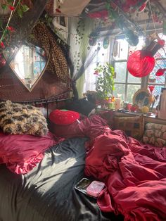 an unmade bed with red sheets and pillows in front of a window, next to a leopard print pillow