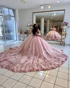 a woman in a pink dress looking at herself in a mirror with flowers on it