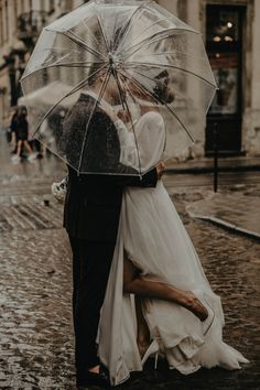 a bride and groom kissing under an umbrella in the rain on their wedding day,