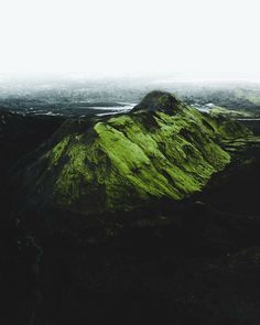 an aerial view of a green mountain in the middle of a valley with water running through it