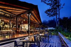 an outdoor dining area with wooden tables and chairs at night, surrounded by greenery