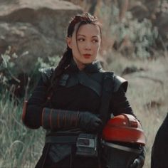 a woman dressed in black holding a red motorcycle helmet and looking off into the distance