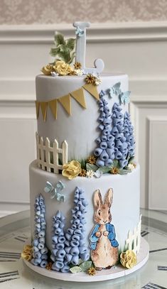 a three tiered cake decorated with blue frosting trees and rabbits on it's sides