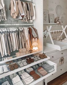 a white closet filled with lots of baby clothes and shoes on shelves next to a dresser