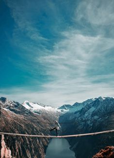 a man walking across a suspension bridge over a lake in the middle of some mountains