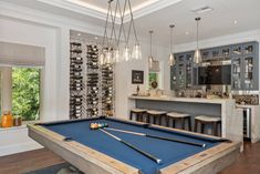 a pool table in the middle of a living room with bar stools and cabinets