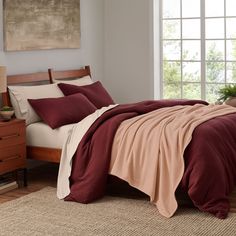 a bed with red and beige sheets in a bedroom next to a window, rugs and dresser