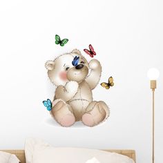 a white teddy bear sitting on top of a bed next to a butterfly wall decal