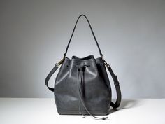 a black leather bucket bag sitting on top of a white table next to a gray wall