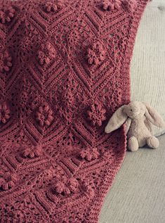 a crocheted blanket with a stuffed animal on the couch next to it's side