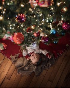 a baby is laying on the floor next to a christmas tree with ornaments around it