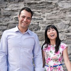 a man and woman standing next to each other in front of a stone wall holding hands