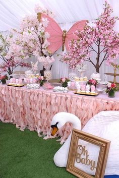 there is a swan sitting on the grass next to a table with pink flowers and desserts