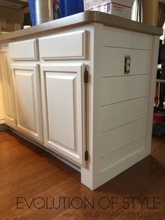 a kitchen island with white painted cabinets and wood flooring in the middle of a room