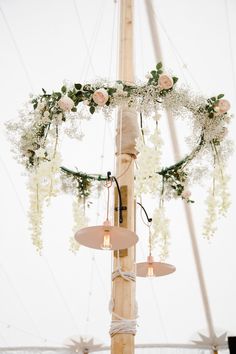 a tall pole with flowers and lights hanging from it's sides in front of a white tent