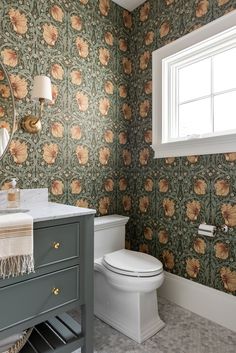 a bathroom with floral wallpaper and a white toilet next to a vanity sink in front of a window