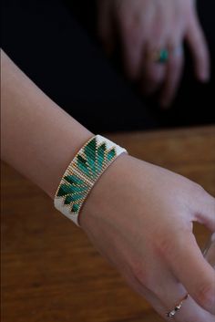 a woman's hand holding onto a cell phone with a green and white bracelet on it