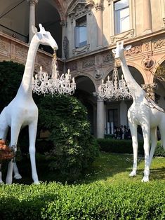 two white giraffe statues in front of a building with chandeliers hanging from it's sides