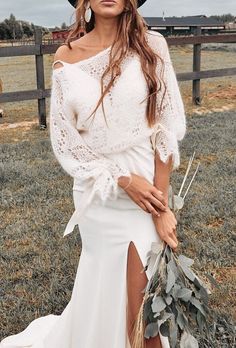 a woman wearing a white dress and black hat posing for a photo in a field