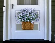 a basket filled with purple flowers sitting on the front door sill next to a white door