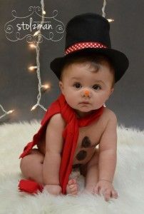 a black and white photo of a baby wearing a top hat, red scarf and orange nose ring