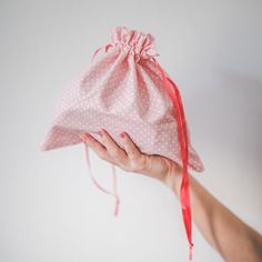 a hand holding a pink bag with white polka dots on it and a red ribbon