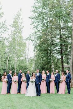 a bride and groom with their bridal party in front of the trees at this outdoor wedding