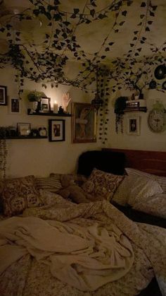 an unmade bed in a room with many pictures on the wall and hanging plants