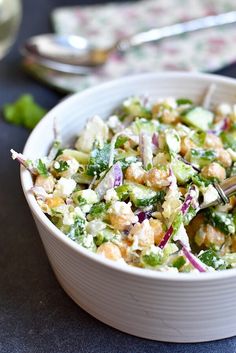 a white bowl filled with salad on top of a table next to silverware and utensils