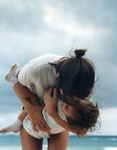 a woman holding a small child on her back at the beach in front of the ocean