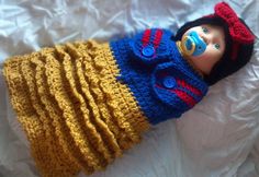 a doll is laying on top of a bed wearing a yellow and blue knitted outfit