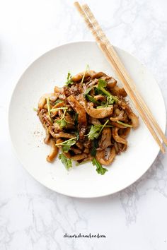 a white plate topped with meat and veggies next to chopsticks