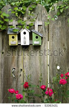 three birdhouses on a wooden fence surrounded by flowers