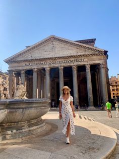 a woman in a white dress and straw hat walking past a building that has columns