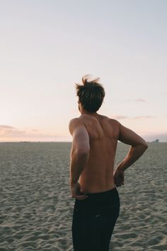 a man standing on top of a sandy beach next to the ocean with his back turned