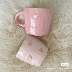 two pink mugs with hearts on them sitting on a white furnishing area