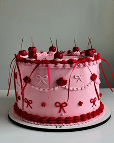 a pink cake decorated with red ribbon and cherries