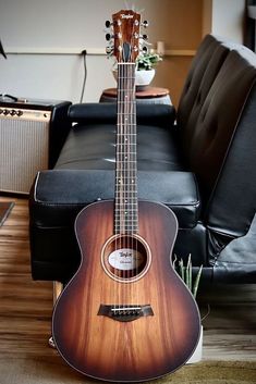 a guitar sitting on top of a hard wood floor next to a black leather couch