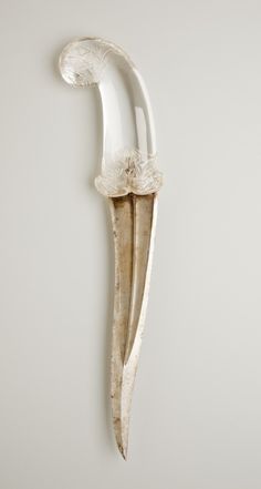 a white wall mounted object with a long blade and flower decoration on it's side