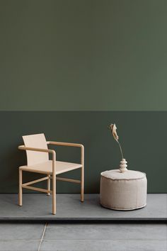 a chair and a table with a flower on it in front of a green wall