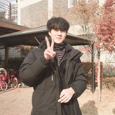 a man standing in front of a building giving the peace sign with his hand while wearing a black coat