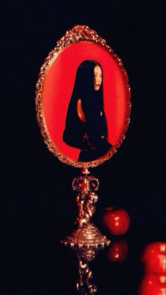 a mirror with a woman's face on it in front of some tomatoes and apples