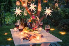 a wooden table topped with wine glasses next to a tree filled with stars and lights