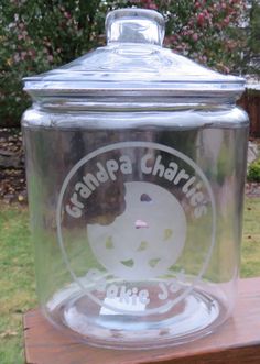 a glass jar sitting on top of a wooden table in front of a garden area