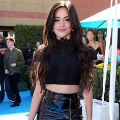 a woman with long dark hair wearing a black top and shiny leather skirt at an event