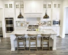 a kitchen island with three stools and two lights hanging over it, in front of an oven