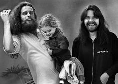 two men with long hair and beards standing next to each other, one holding a small child