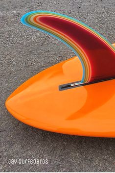 an orange surfboard sitting on the ground with its fin sticking out from it's side