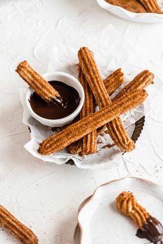 some churro sticks are on a plate with dipping sauce in the bowl next to them