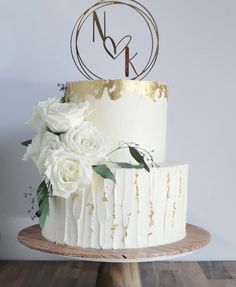 a wedding cake with white flowers on top and gold foiling around the edges, sitting on a wooden stand